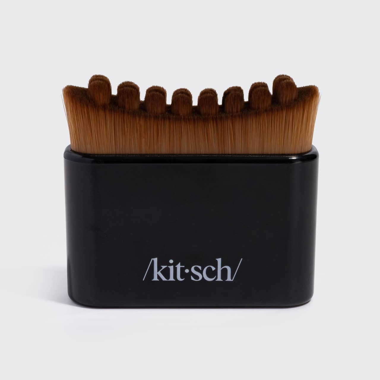 A Kit-Sch grooming brush with brown bristles and a black handle, featuring the Kit-Sch logo on the front, set against a plain light gray background.